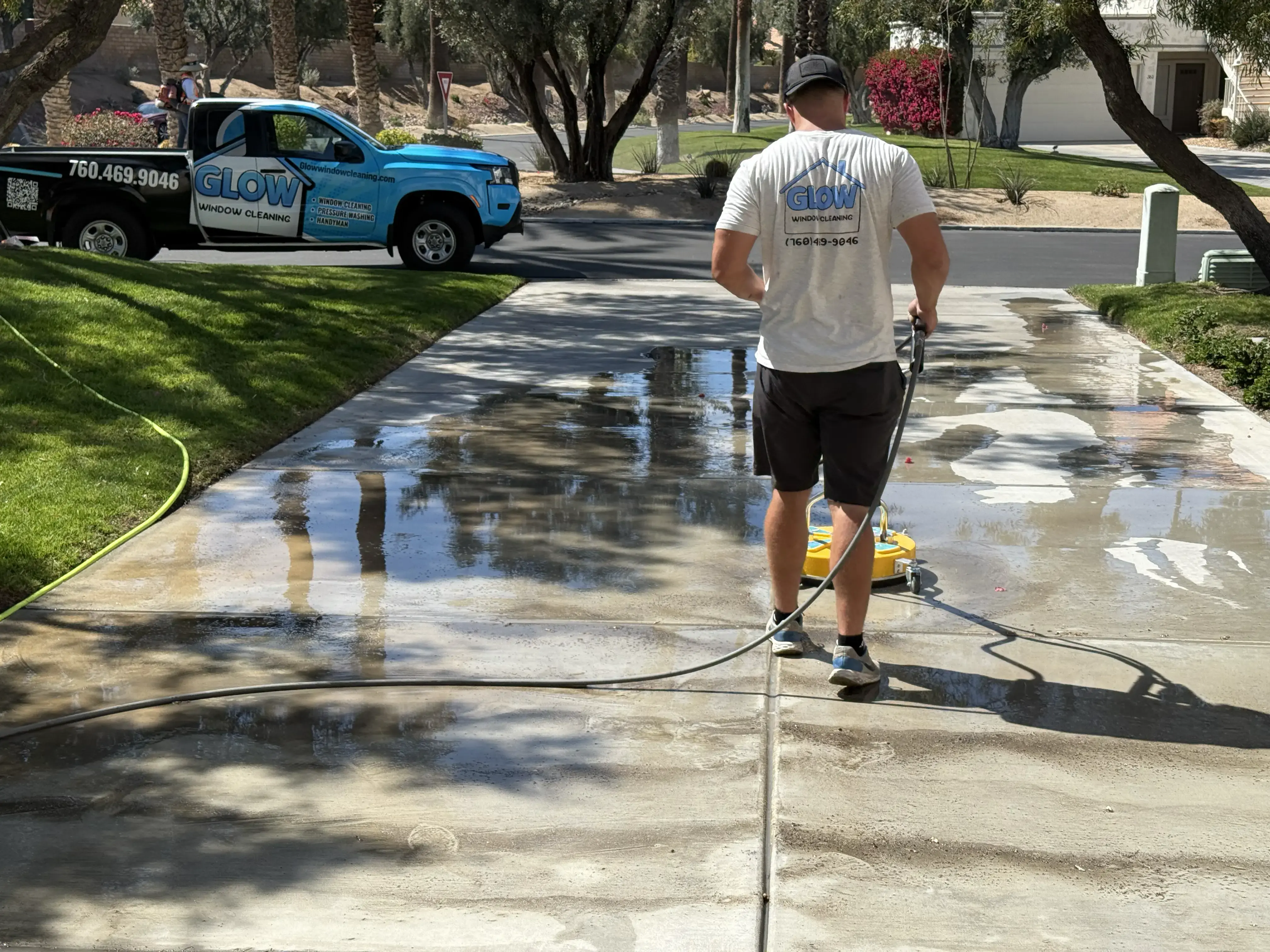 Glow technician pressure washing a driveway with professional equipment.